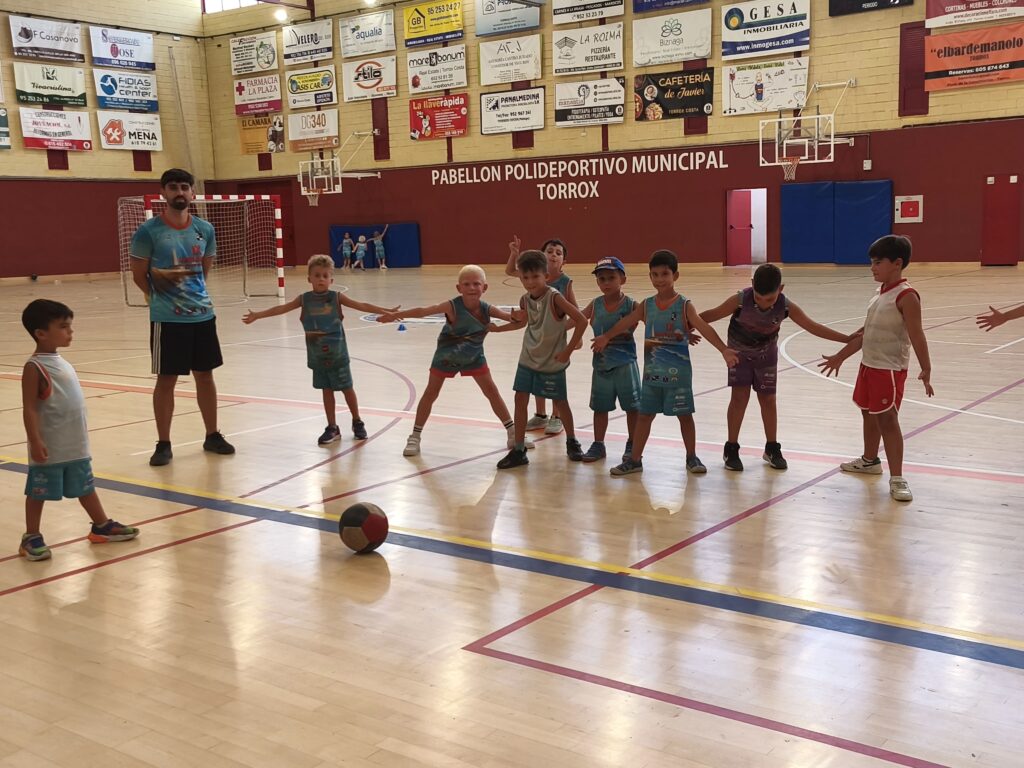 Niños en pose de defensa de baloncesto en campamento deportivo torrox
